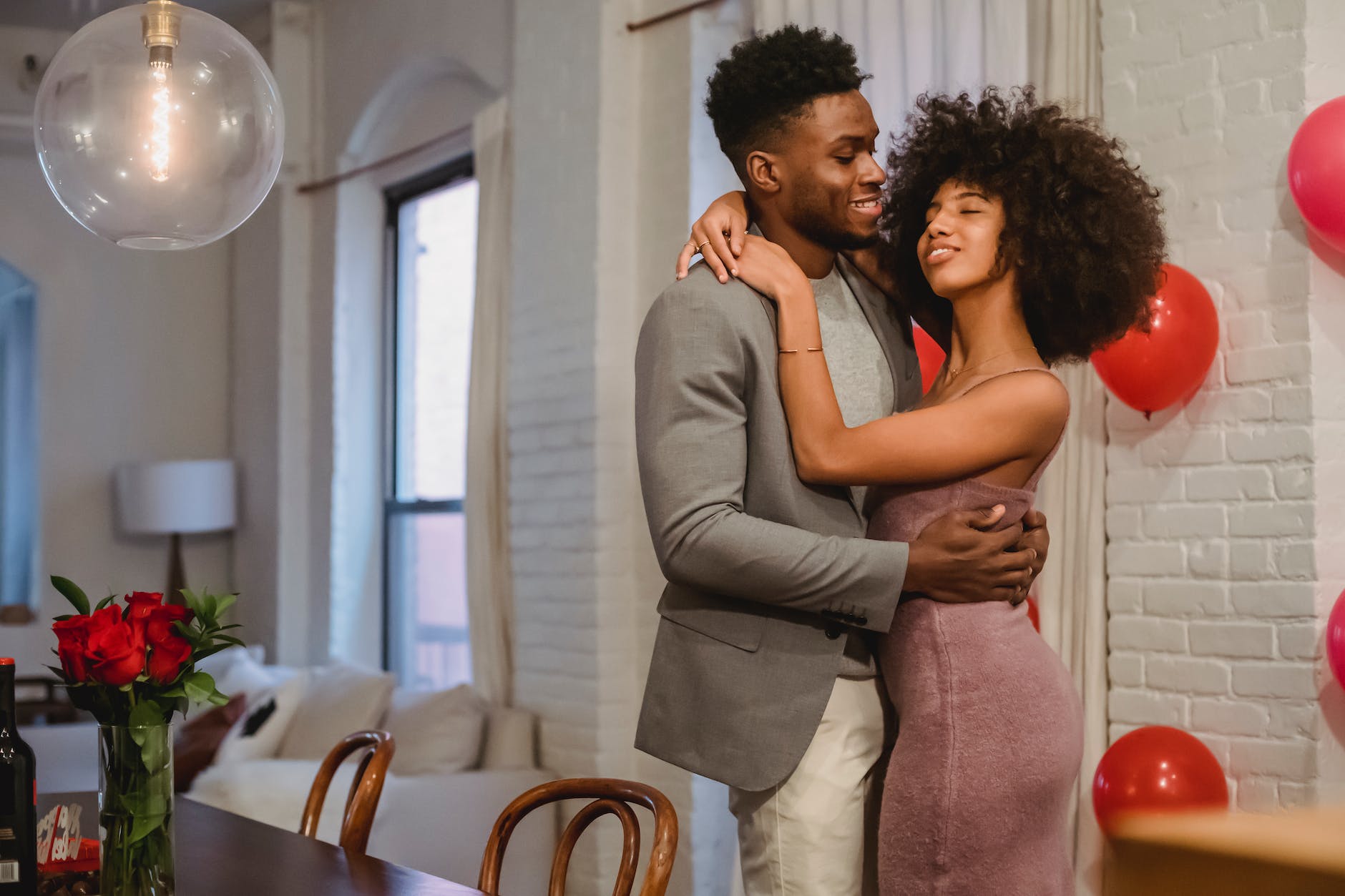 positive black couple dancing while hugging in room near table